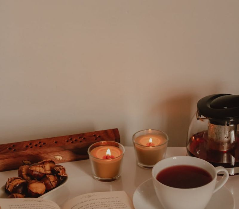 A cozy corner with a lit candle, a book, and a warm cup of herbal tea.