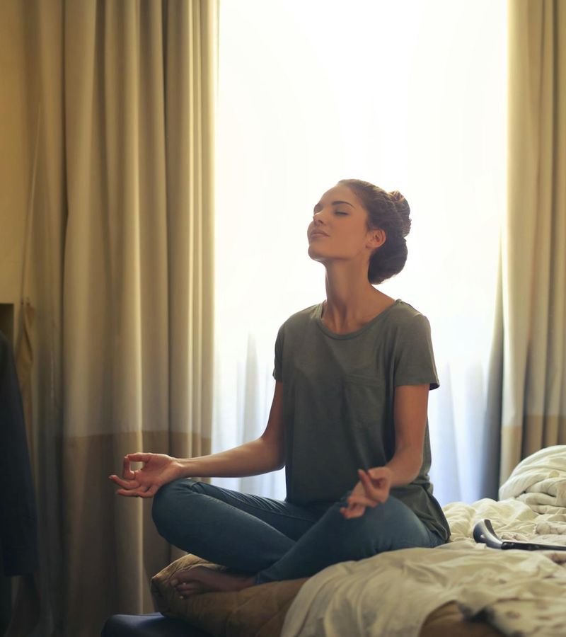Woman sitting in a calm, meditative pose by a window at dusk.